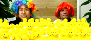 Two men in wigs with yellow smiley faces

Description automatically generated