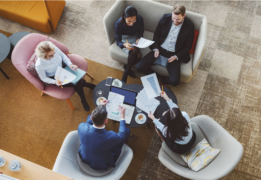 overhead view of five team members sitting in chairs talking and reviewing documents